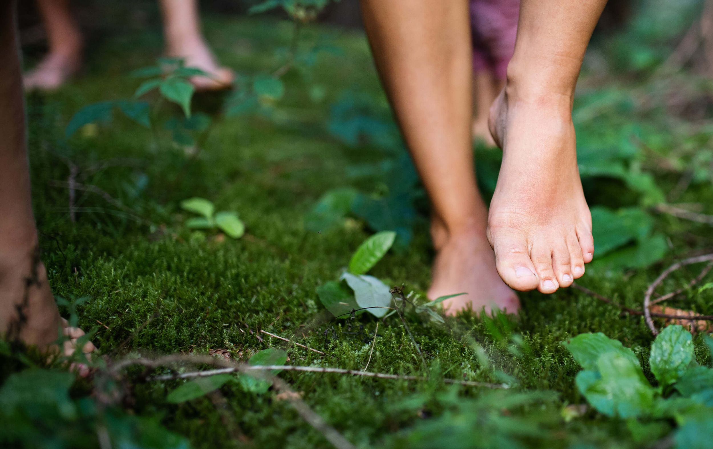 Barfuß gehende Füße auf moosbedecktem Waldboden zwischen grünen Pflanzen.